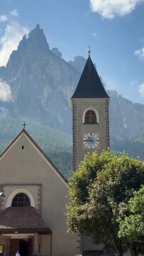 Historic church tower in Siusi allo Sciliar with dramatic Dolomite peaks in the background, near Alpe di Siusi, Italy. Authentic alpine village, slow living and rural travel scene