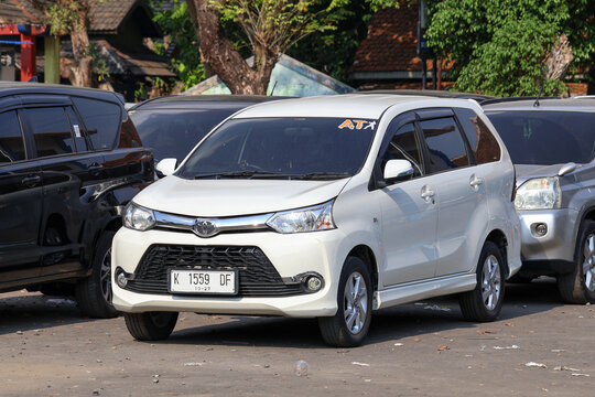 A white Toyota Avanza TRD Sportivo minivan parked on the side of a street near local shops and outdoor activities.