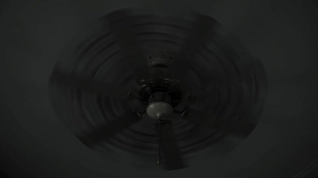 A dark ceiling fan spinning slowly.