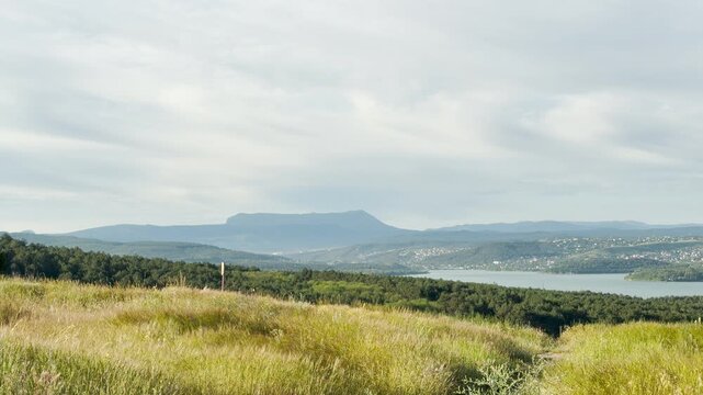 A majestic mountain stands on the distant horizon past a wide reservoir. Wild grass gently sways on the peaceful hillside, bringing a deep feeling of calm and serene beauty.