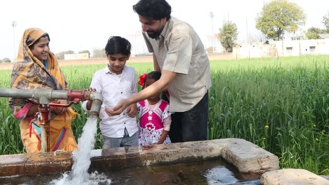 Indian farmer family drinking fresh water from tube well irrigation pipe in agricultural field, rural life, farming, groundwater, water supply,, India. 