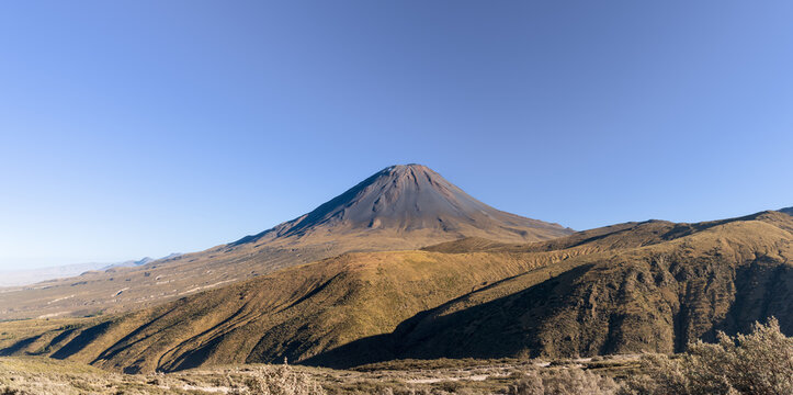The majestic symmetrical cone of El Misti volcano rises behind rolling, sunlit arid mountain ridges under a vast clear blue sky near Arequipa, Peru.