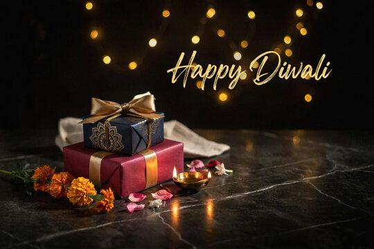 Happy Diwali greeting card with gift boxes, traditional oil lamp diya and marigold flowers on dark marble background, festive celebration banner