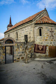 Ancient stone Orthodox church with red tiled roof, domed steeple, and traditional rug in Tbilisi, Georgia.