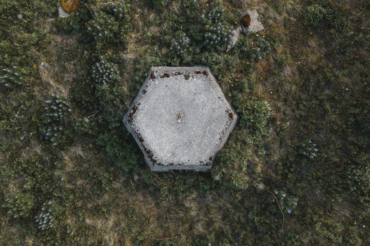 Aerial view of a historic hexagonal concrete bunker surrounded by wild vegetation and wildflowers in Unalaska, Alaska, United States.