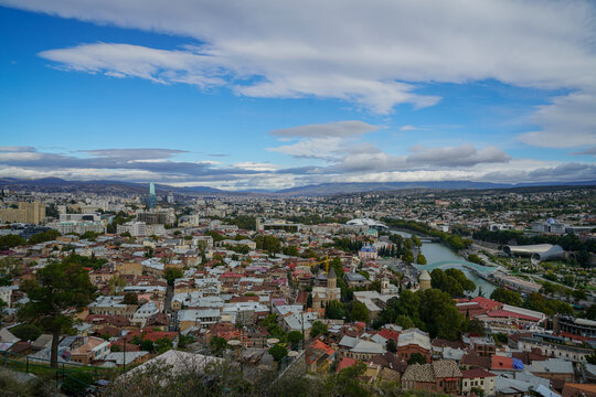 Expansive aerial view of Tbilisi, Georgia, featuring Mtkvari River, Peace Bridge, and Sameba Cathedral.