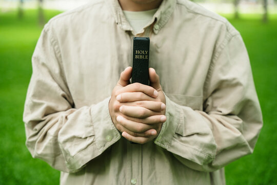 The concept of reading the Bible and praying to God for blessings, living peacefully in nature and spending time with God, with a hand holding a Bible.