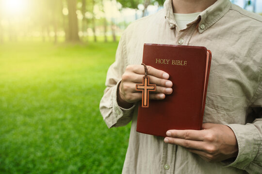 The concept of reading the Bible and praying to God for blessings, living peacefully in nature and spending time with God, with a hand holding a Bible.