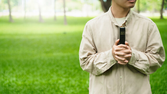 The concept of reading the Bible and praying to God for blessings, living peacefully in nature and spending time with God, with a hand holding a Bible.