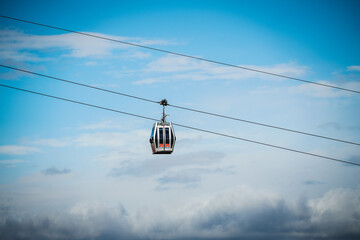 Modern cable car cabin transporting passengers above Tbilisi city, Georgia, against a bright blue cloudy sky © Greggory Zzyzx