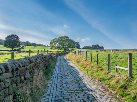 Spencer lane, a cobbled narrow country lane near Hebden Bridge in West Yorkshire surrounded by grass covered meadows in summer sunshine