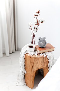 Bedside decor with alarm clock, cotton branch, book, coffee in bedroom. Minimalist home interior and healthy sleep routine. Concept of biological clock, circadian rhythm, digital detox
