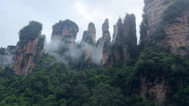 Tall karst Avatar mountain pillars rising above forest valley covered mist. Natural rock formation landscape, Zhangjiajie Wulingyuan park. Scenic view majestic sandstone cliffs for travel background.