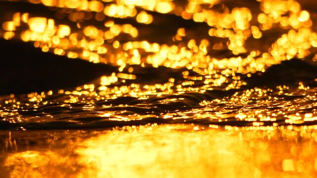 Water reflection gold ripples flowing in sunlight at sunset creating a peaceful and shimmering nature background with beautiful bokeh light effects