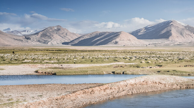 Clear-water rivers and lakes in a mountain valley, pastures and green grassy fields set against mountain ranges and snow-capped, glacier-clad peaks&mdash;a scenic landscape background