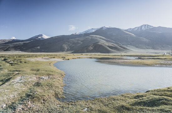 Clear-water rivers and lakes in a mountain valley, pastures and green grassy fields set against mountain ranges and snow-capped, glacier-clad peaks&mdash;a scenic landscape background