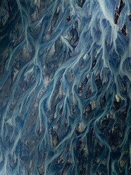Aerial view of the intricate patterns of a glacial braided river flowing through the volcanic landscape of Iceland.