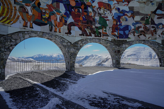 Colorful mosaic mural and stone arches frame snowy Caucasus Mountains at Gudauri Viewpoint, Georgia.