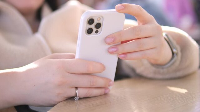 Hands scroll phone at table, sunlit. Fingers tap screen, calm focus. Perfect for digital life, cafe, work, leisure scenes
