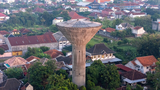 Aerial view of Menara Air Jonggrangan surrounded by residential rooftops and lush trees in Kecamatan Klaten Utara, Jawa Tengah, Indonesia.