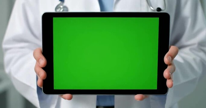 Doctor holding tablet with green screen for medical presentation or application display.