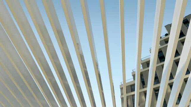 White canopy slats frame a clear blue sky in Simferopol, Crimea. A modern building rises quietly in the background. This clean geometric view brings a deeply calm and peaceful feeling.