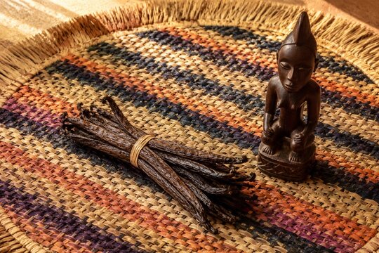 A handwoven raffia table mat with vanilla pods and a wooden carving.