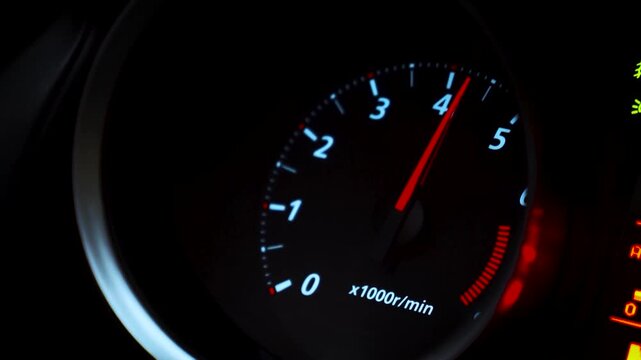 Dynamic close-up of a glowing car tachometer needle rising rapidly during acceleration, showcasing the illuminated digital display and high-performance automotive dashboard
