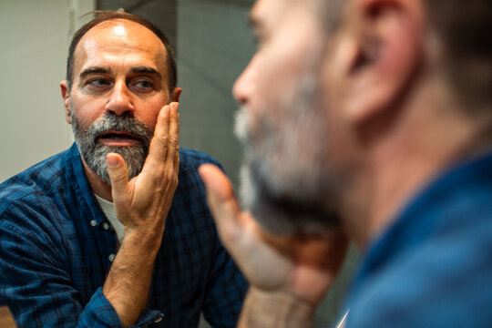 Bearded middle-aged man checking skin in bathroom mirror