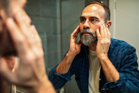 Mature bearded man checking skin in bathroom mirror