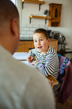 Parent helping young boy with homework at kitchen table