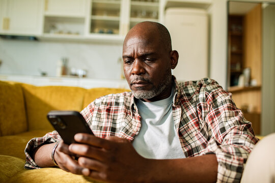 Mature man using smartphone on sofa at home