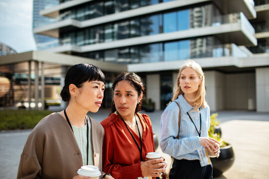 Three businesswomen networking with coffee outside modern office