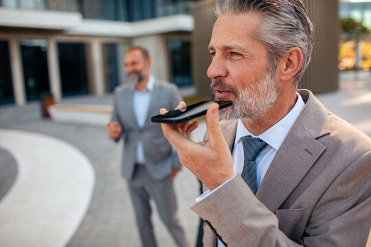 Senior businessman using voice assistant outside office