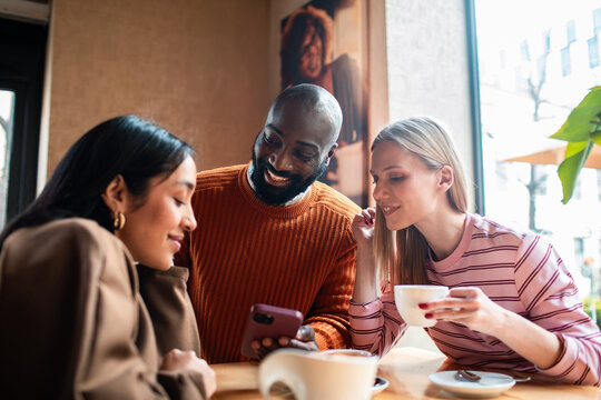Three friends sharing a smartphone at a cafe table