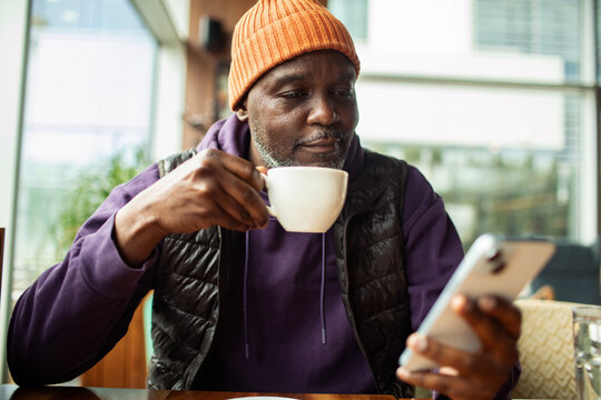 Mature man drinking coffee and using smartphone at cafe