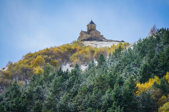 Gergeti Trinity Church perched above snowy autumn forest in Stepantsminda, Georgia under clear sky