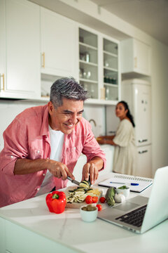 Middle-aged man chopping vegetables while following an online recipe in a home kitchen