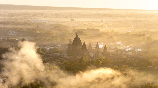 Aerial view of the ancient Prambanan Temple complex surrounded by morning mist and golden sunlight in Indonesia.