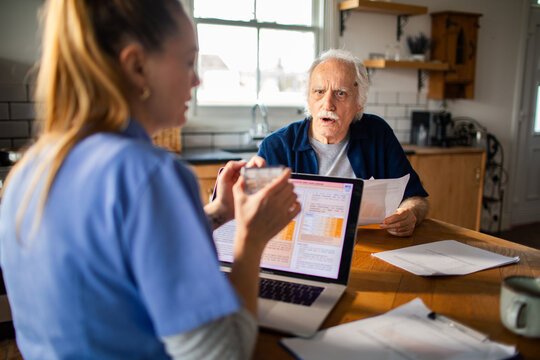 Home care nurse reviewing medical paperwork with senior man in kitchen