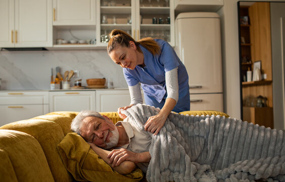 Caregiver tucking elderly man in on sofa at home