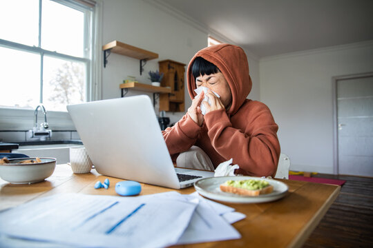 Sick person sneezing while working from home in kitchen