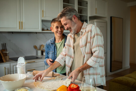 Mature couple making homemade pizza dough in modern kitchen