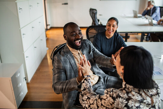 Diverse coworkers celebrating success with high five in modern office
