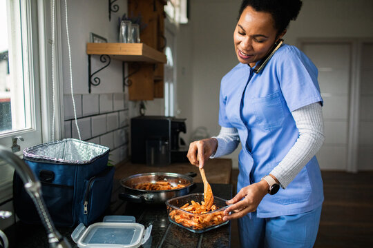 Nurse packing pasta lunch in home kitchen while on phone