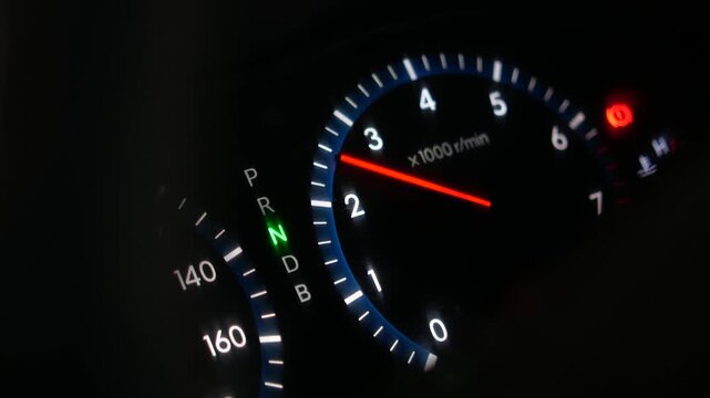 Detailed view of a car instrument cluster featuring a glowing tachometer and gear selector display while the engine is running in neutral at night, high quality.