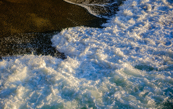 High angle view of white ocean waves crashing onto a dark sandy beach with natural coastal beauty