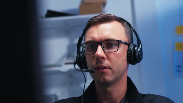 Male Tech Support Professional Providing Customer Assistance, Helping a Client Resolve Problem Troubleshooting and Technical Problem Resolution Through Headset and Computer at desk in office.