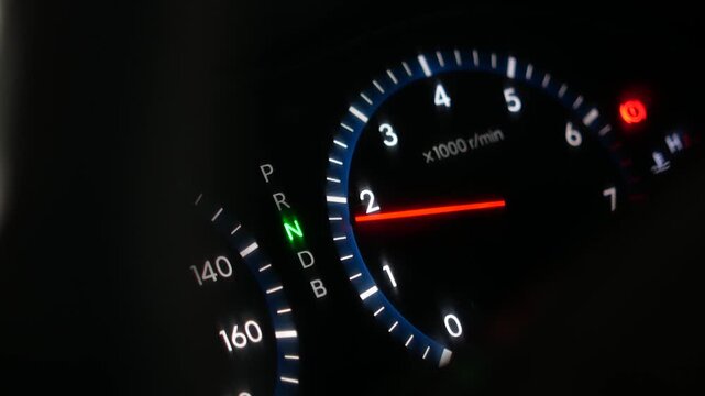 Macro shot of a vehicle dashboard showing the tachometer and gear indicator in neutral, capturing the glowing lights and mechanical precision of a modern car.