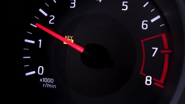 Close up of a car dashboard tachometer with a warning key light illuminated, showing the engine speed increasing while driving in a modern vehicle at night time.